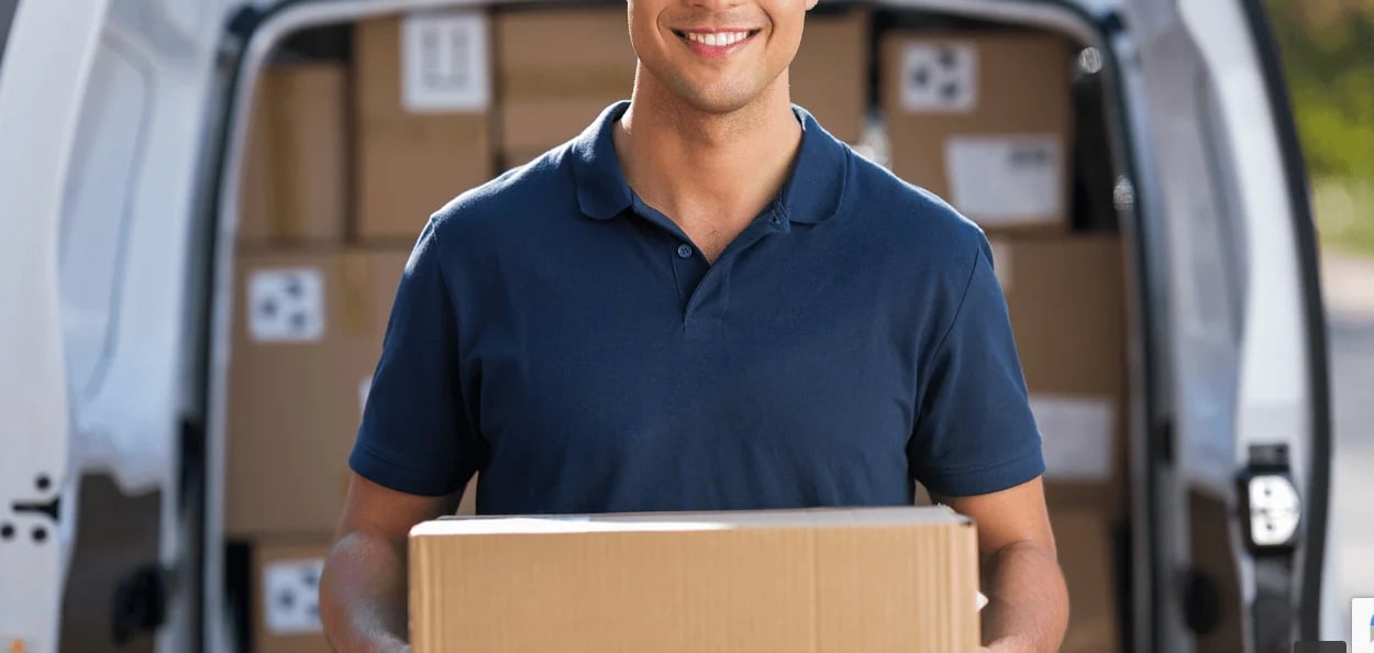 Delivery worker in navy shirt holding cardboard box in front of van loaded with packages